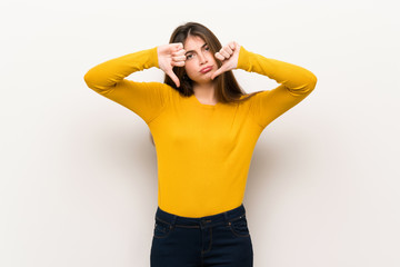 Young woman with yellow sweater showing thumb down with both hands