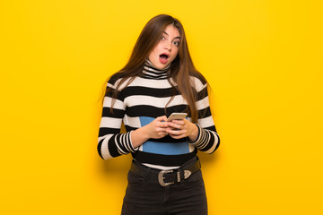 Young woman over yellow wall surprised and sending a message