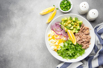 Salad with tuna, avocado, onion, egg and lemon. Spring healthy delicious lunch on light background