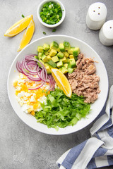 Salad with tuna, avocado, onion, egg and lemon. Spring healthy delicious lunch on light background