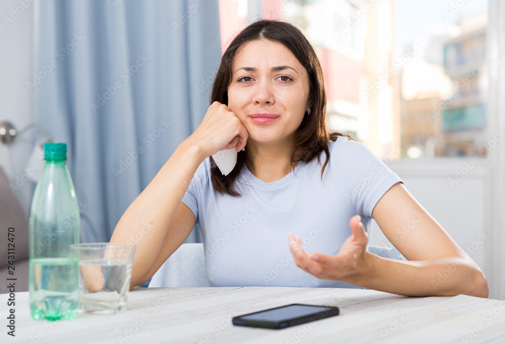 Wall mural upset girl suffering from troubles at table with bottled water