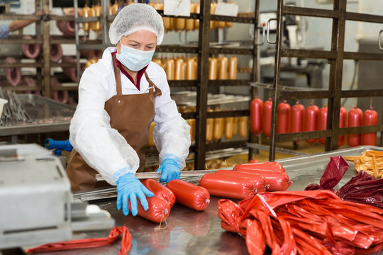 Workwoman hanging up sausages on racks