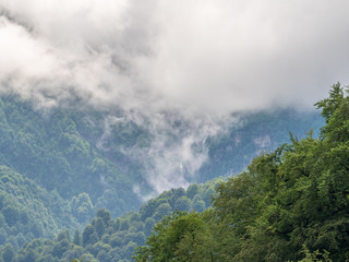 Majestic view of green mountains with a waterfall and peaks in thick fog