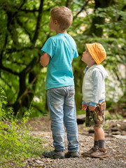 Two boys, 3 years and 7 years old on the path in the green forest look one way