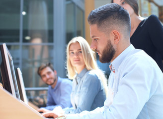Group of young people in casual wear sitting at the office desk and discussing something while looking at PC together.