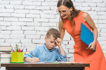 Student boy doing difficult work in school supervised by his teacher