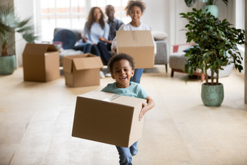 Cute happy mixed race children enjoying moving day running carrying holding boxes, excited african...