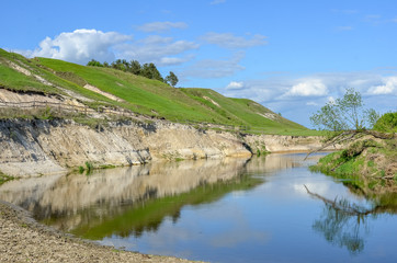 Spring countryside scenery with green hills and sky reflected in blue water surface.