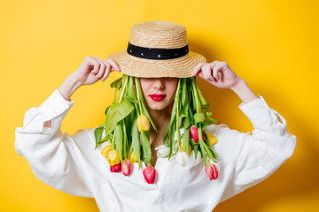 Beautiful woman in white shirt and hat with fresh springtime tulips instead hair on yellow background