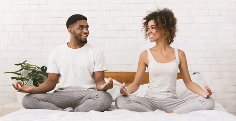 Young black family meditating in bed together