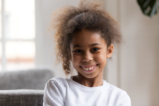 Cute funny little african american girl looking at camera, smiling mixed race child posing for portrait at home, preschool positive black kid with happy face headshot, orthodontic malocclusion