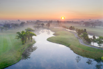 Aerial view Green Golf course with sunset and fog in the morning.