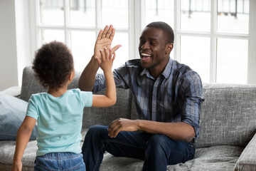 Happy black dad and little son giving high five playing at home, excited african single father and toddler cute kid boy laughing enjoying clapping hands having fun together, daddy child friendship - obrazy, fototapety, plakaty