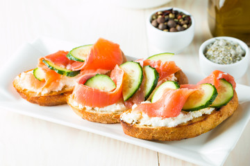 Salmon, cucumber and cream cheese bruschetta. Italian tapas, antipasti with vegetables, herbs and oil on grilled ciabatta and baguette bread. Sandwich.