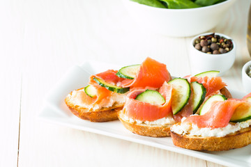 Salmon, cucumber and cream cheese bruschetta. Italian tapas, antipasti with vegetables, herbs and oil on grilled ciabatta and baguette bread. Sandwich.