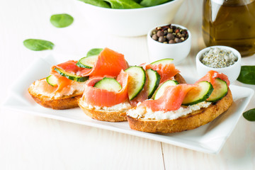 Salmon, cucumber and cream cheese bruschetta. Italian tapas, antipasti with vegetables, herbs and oil on grilled ciabatta and baguette bread. Sandwich.