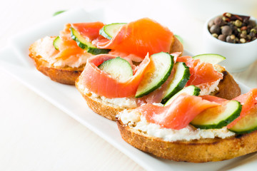 Salmon, cucumber and cream cheese bruschetta. Italian tapas, antipasti with vegetables, herbs and oil on grilled ciabatta and baguette bread. Sandwich.