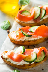 Salmon, cucumber and cream cheese bruschetta. Italian tapas, antipasti with vegetables, herbs and oil on grilled ciabatta and baguette bread. Sandwich.