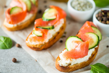 Fototapeta na wymiar Salmon, cucumber and cream cheese bruschetta. Italian tapas, antipasti with vegetables, herbs and oil on grilled ciabatta and baguette bread. Sandwich.