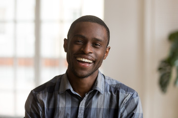 Cheerful african american millennial man with happy face looking at camera at home, head shot of smiling young black single guy laughing posing indoors, confident charming male person portrait