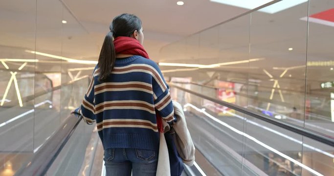 Woman taking escalator inside shopping mall