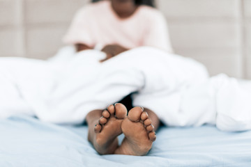 girl sticked her legs out of white blanket. focus on naked legs black legs. close up photo