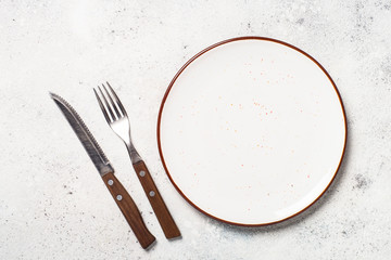 White craft plate, cutlery and napkin on white stone table. 