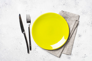 Green plate, cutlery and tablecloth on light stone table.