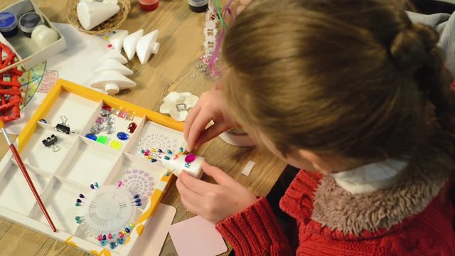 
Child girl is making decoration for holidays. Crafts and toys, christmas tree and other. Painting watercolors. Top view. Artwork workplace with creative accessories. Flat lay art tools.