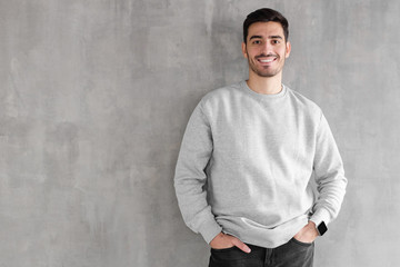 Young man in oversized sweatshirt isolated on textured gray wall background with copy space for...