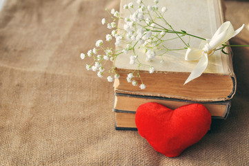 Vintage rustic love card for Valentine's day-white flowers, yellowed old books and red plush heart on burlap. closeup. tinted. Shabby chic