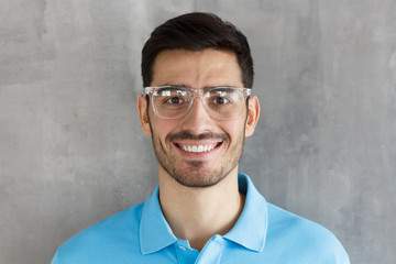 Close up portrait of young smiling handsome guy in blue polo shirt and round glasses, standing...