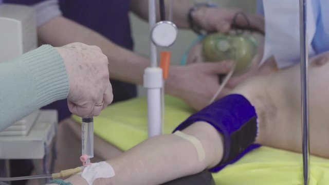Injection by syringe with medicine during the general anesthesia making to an unidentified wooman lying on a surgical table while anesthesiologist presses a mask to her face (4K, 25fps)