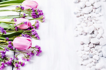 Pink flowers and white pebbles on a white wooden background