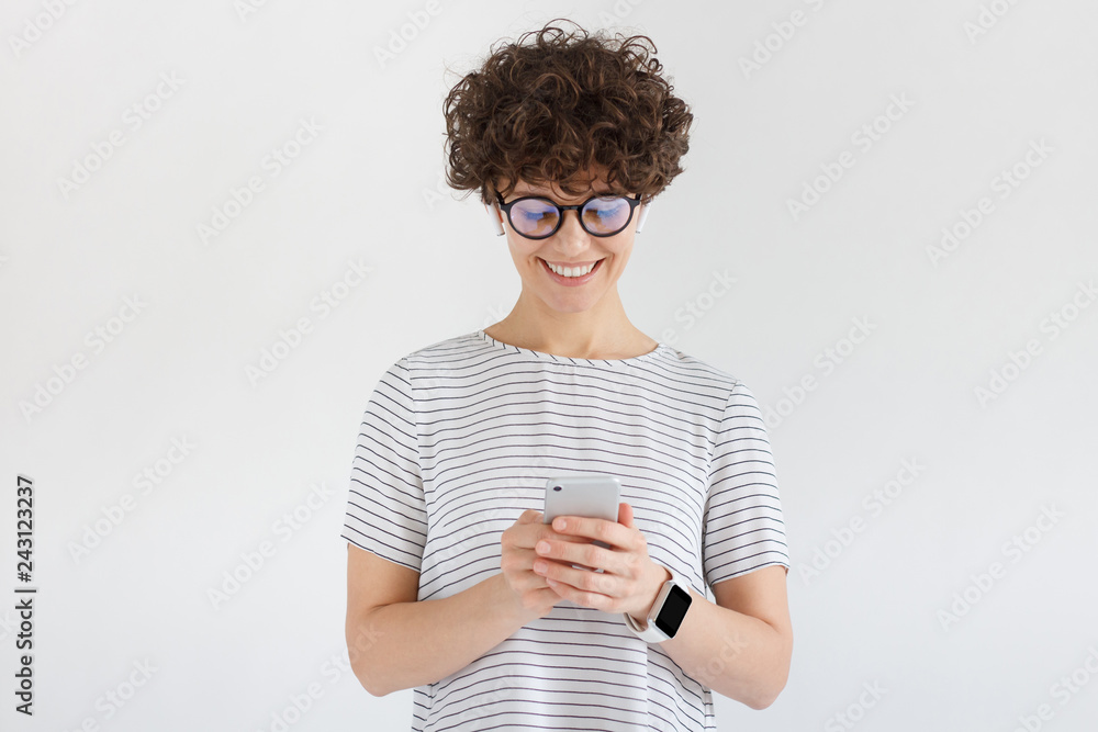 Wall mural young female looking at screen of phone with smile, browsing web pages or chatting with friend, stan