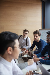 Fototapeta premium Positive young multiracial male team sitting at conference meeting table listening to speaker presenting new project in office, Business Team Meeting Brainstorming Togetherness Concept.