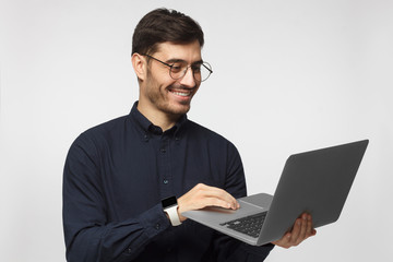 Portrait of young business man standing, holding laptop with happy smile