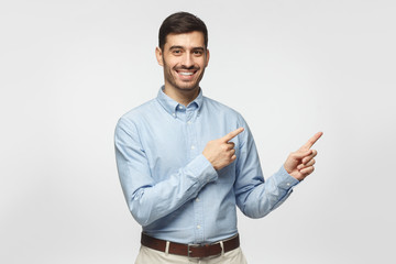 Happy smiling young business man pointing away, isolated on gray background