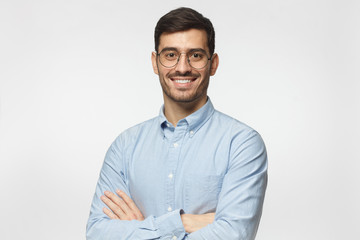 Modern businessman in blue shirt standing with crossed arms, isolated on gray background