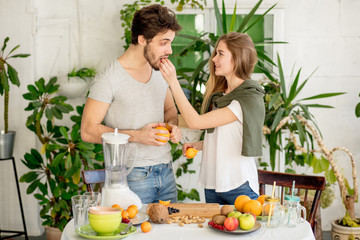 awesome couple are eating oranges at home. vitamins, body and health care. green flowers on the bcakground of the photo