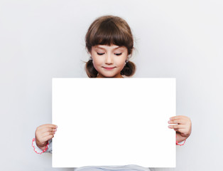 The little girl is holding a blank sheet of paper. Education. Advertising. Copy space. Place for text.