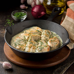 Chicken fillet or Turkey breast in creamy sauce with dill and garlic, in cast iron black pan on dark background. Delicious homemade food