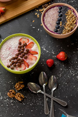 delicious dairy dessert with berries and nuts. two bowls with yoghurt and teaspoons on the black table