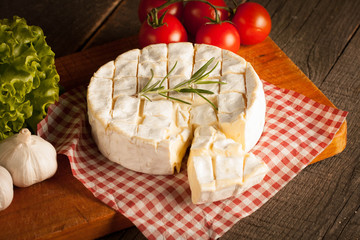Camembert and brie cheese on wooden background with tomatoes, letuce and garlic. Italian food. Dairy products.