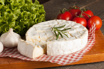 Camembert and brie cheese on wooden background with tomatoes, letuce and garlic. Italian food. Dairy products.