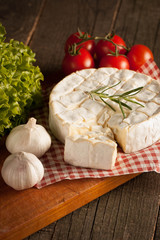 Camembert and brie cheese on wooden background with tomatoes, letuce and garlic. Italian food. Dairy products.