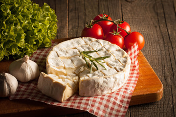 Camembert and brie cheese on wooden background with tomatoes, letuce and garlic. Italian food. Dairy products.