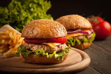 Home made hamburger with beef, onion, tomato, lettuce and cheese. Fresh burger close up on wooden rustic table with potato fries, beer and chips. Cheeseburger.