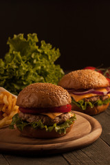 Home made hamburger with beef, onion, tomato, lettuce and cheese. Fresh burger close up on wooden rustic table with potato fries, beer and chips. Cheeseburger.
