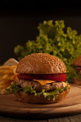 Home made hamburger with beef, onion, tomato, lettuce and cheese. Fresh burger close up on wooden rustic table with potato fries, beer and chips. Cheeseburger.